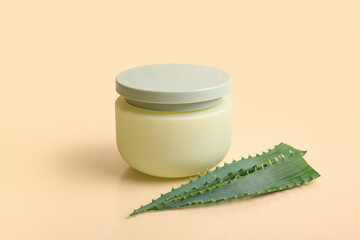 Jar of cosmetic cream with aloe vera leaves on beige background