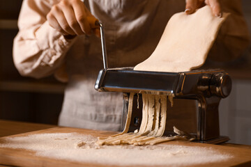 Young woman making pasta with machine at table in dark kitchen, closeup