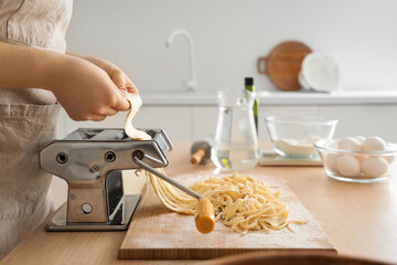 Young woman making pasta with machine at table in kitchen