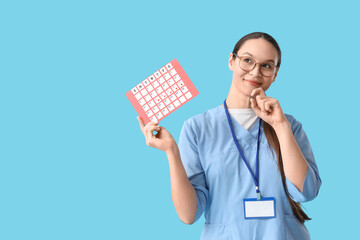 Thoughtful female doctor with menstrual calendar on blue background