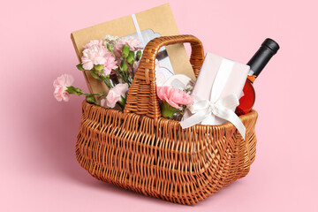 Gift basket with spring flowers, wine, candies and cosmetics on pink background
