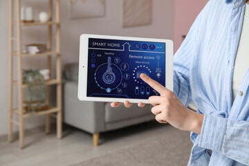 Young woman pointing at tablet with smart home security system control panel in room, closeup