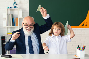 Happy kid in school break. Senior teacher with pupil with paper plane in school classroom. Education, elementary school. School break. Teacher with pupil with airplanes. Education concept.