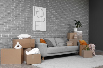 Stylish poster and sofa with cardboard boxes in room on moving day