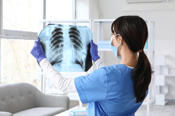 Female doctor with x-ray scan of lungs in clinic, back view