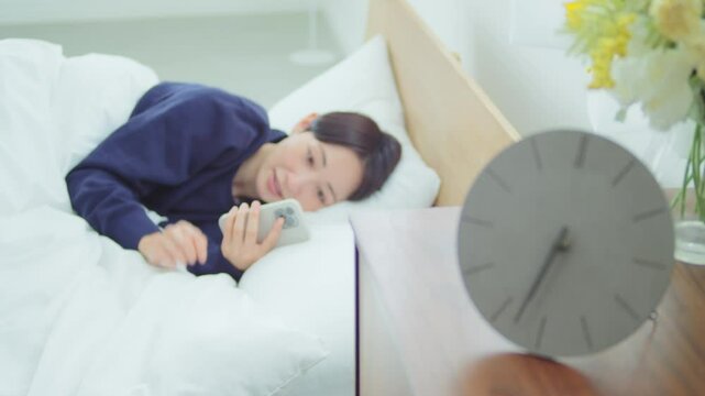 ベッドでスマートフォンを操作する女性