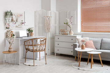 Interior of light office with workplace, pegboard and blossoming branches in vases
