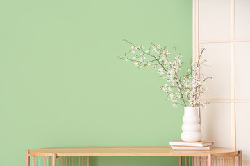 Folding screen and blooming tree branches on wooden table near green wall