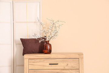 Folding screen and blooming tree branches on dresser near beige wall