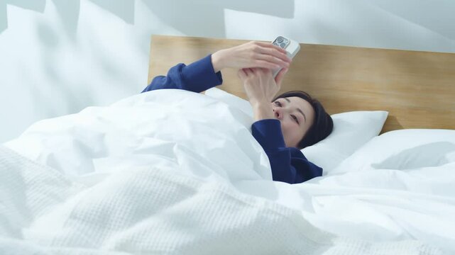 ベッドでスマートフォンを操作する女性