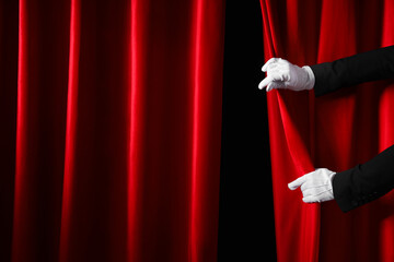 Female hands in white gloves opening red curtains on dark background