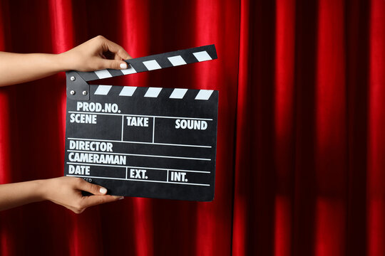 Female hands with movie clapper against red curtain