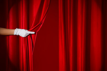 Female hand in white glove opening red curtain on color background
