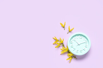 Alarm clock and flowers on lilac background. Spring time