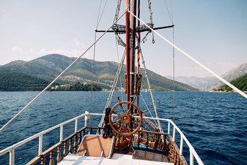 Bow of a wooden ship with steering wheel near the mast sailing on the sea