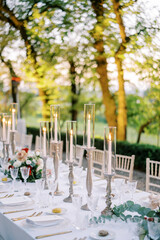 Festive table with lit candles and bouquets of flowers in the garden