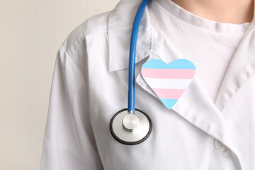Female doctor with paper heart in colors of transgender flag on light background, closeup
