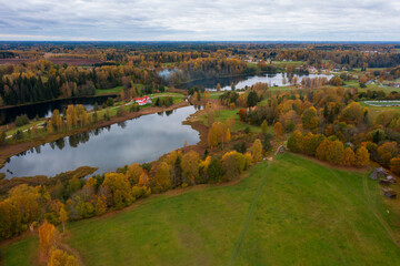 Aerial View of Autumn Landscape with Serene Lake and Colourful Forest. Dramatic Cloudy Sky Over Fall Countryside with Golden Trees, Green Fields and Peaceful Lakefront