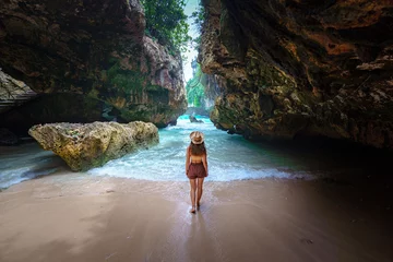 Fototapeten Bali Back of girl traveler wearing hat on the beach among the rocks on Bali island. Journey to a beautiful destination  © Goffkein