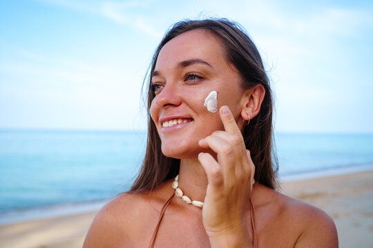 Portrait of tanned happy satisfied smiling young brunette woman with spf sunscreen lotion on face. Uv protection and skin care, healthy skin