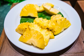 Sliced pineapple served on a white plate with a green leaf as garnish, creating a refreshing and tropical presentation