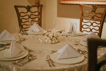 Elegant dinner table setting with white roses centerpiece,  fine china, silverware, and napkins. Perfect for wedding, event or restaurant promotion.