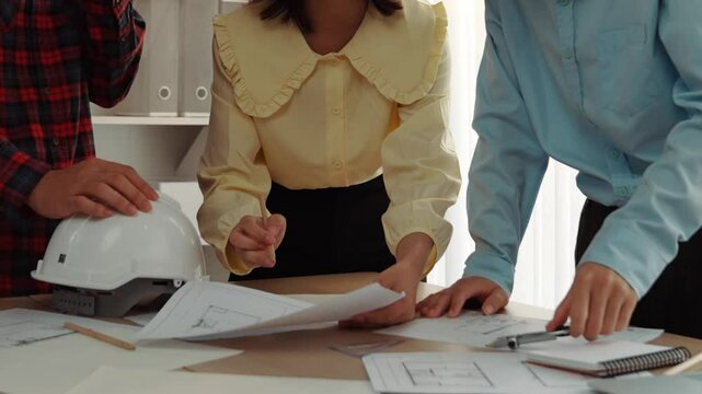 Architect and safety engineer discussion about building blueprint displaying on laptop on table with architectural document and wooden block scatter around at modern office. Closeup. Delineation.