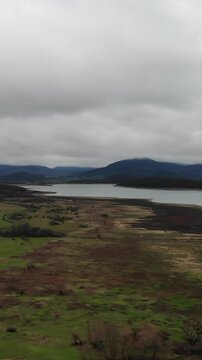 Village on plateau on cloudy sky landscape from landing flying drone. Aerial view of lake in the foothills. Mountain peaks in the background on fogy sky.