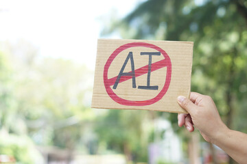 Close up hand holds paper card with No AI,  prohibition sign, outdoor nature background. Concept,...