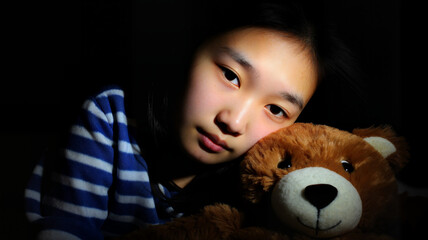 Sad child hugging teddy bear in dimly lit room  