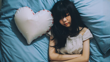 Young woman expressing sadness on a bed with heart pillow  