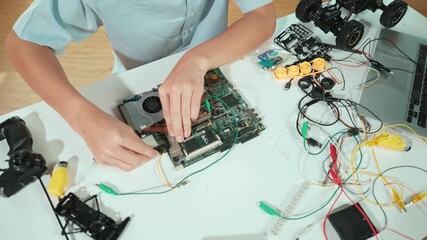 Closeup of boy hand fixing motherboard with electronic tool on table. Top view of high school student repair electric board with electronic equipment, wires tool scatter around on table. Edification