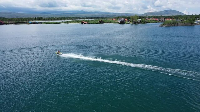 Bird's-eye view of a jet ski moving across the open waters of Lake Sevan with a white trail behind
