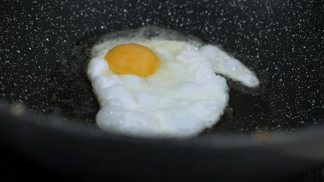Cooking fried eggs sunny side up with a sizzling oil in frying pan.