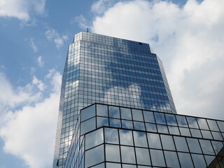 Modern Glass Office Tower with Angled Corners Reflecting Blue Sky and White Clouds