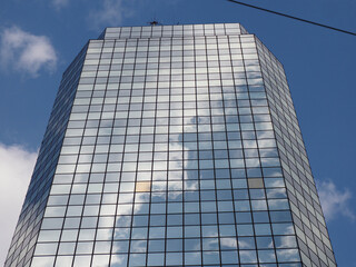 Fototapeta premium Reflective Glass Skyscraper with Geometric Facade Pattern Capturing Blue Sky and Clouds