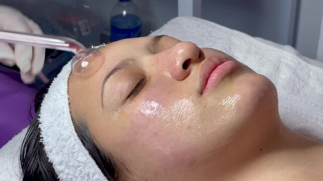 Video of a young Colombian mestiza woman in a beauty spa where she has a facial cleansing and goes through the purification step with a facial microcurrent device.