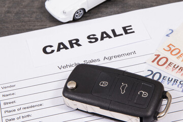 White toy car, car key, euro banknotes and vehicle sales agreement. Inscription car sale. Sales,...