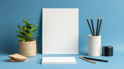 A clean and modern workspace mockup features a blank vertical poster, business cards, pencils in a holder, a small plant, and a blue background ideal for design presentations.
