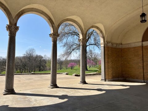Shadows cast by arched pavilion onto spring lawn with blooming trees