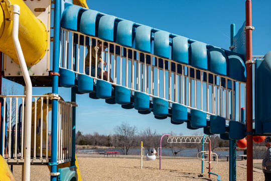 boy playing on a colorful playground with father nearby  watching