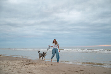 woman walking barefoot with her dog on beach of North sea, Denmark