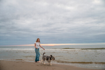 woman walking barefoot with her dog on beach of North sea, Denmark