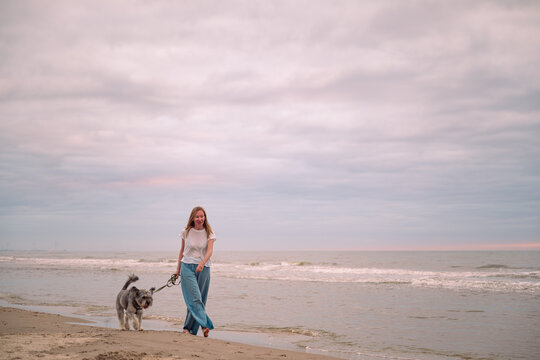 woman walking barefoot with her dog on beach of North sea, Denmark