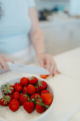 Health influencer slicing strawberries beside white bowl.