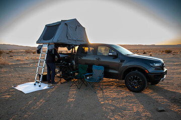Rooftop tent setup at desert campsite during sunrise light.