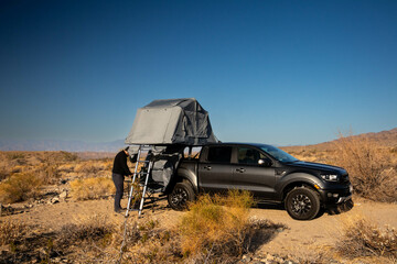 Man setting up rooftop tent on truck in desert landscape.