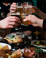 friends hands cheers beer together in a restaurant with food