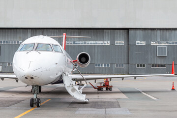 Regional aircraft with an opened gangway door at the airport near airplane hangar