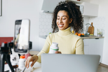 Side view of cheerful black female blogger nutritionist live-streaming talking to her followers...